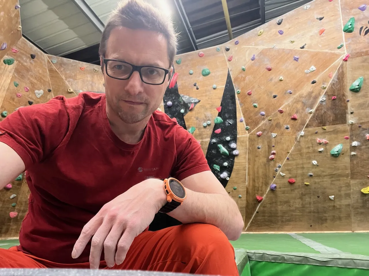 A picture of me sat relaxed infront of a plywood climbing wall.